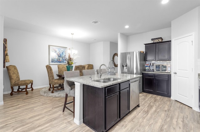 kitchen featuring a kitchen island with sink, hanging light fixtures, sink, appliances with stainless steel finishes, and a notable chandelier