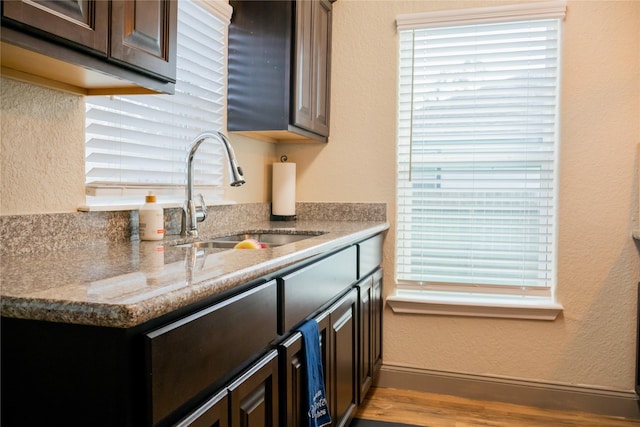 kitchen with light stone countertops, dark brown cabinetry, and sink