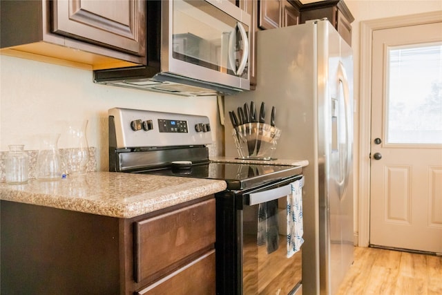 kitchen featuring appliances with stainless steel finishes, dark brown cabinetry, light hardwood / wood-style floors, and light stone counters