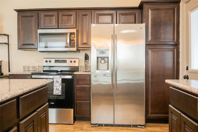 kitchen with light stone countertops, light hardwood / wood-style flooring, dark brown cabinets, and appliances with stainless steel finishes