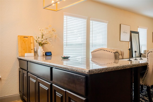 interior space with kitchen peninsula, light stone countertops, and dark brown cabinets