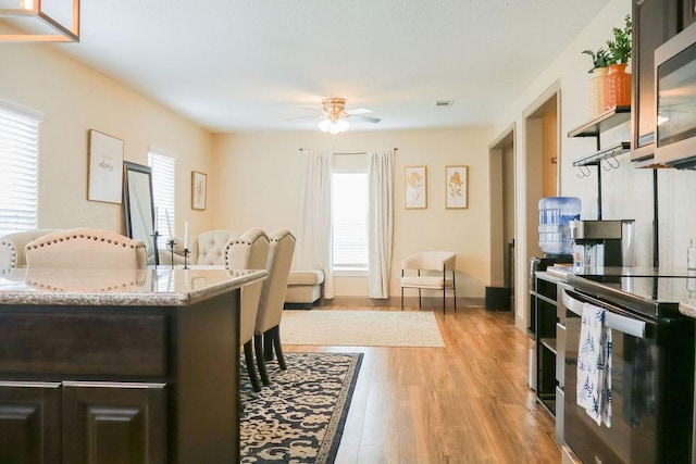 interior space with a breakfast bar, ceiling fan, light wood-type flooring, dark brown cabinetry, and stainless steel appliances