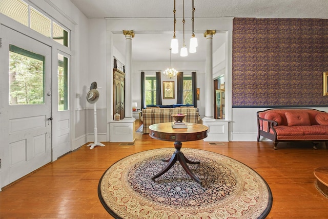 entrance foyer featuring hardwood / wood-style floors, a textured ceiling, ornate columns, and a notable chandelier