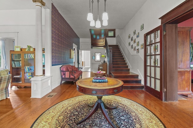 foyer with ornate columns, wood-type flooring, a textured ceiling, and a notable chandelier