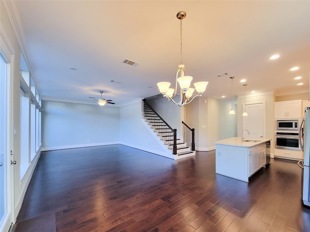 kitchen with appliances with stainless steel finishes, sink, pendant lighting, white cabinetry, and an island with sink