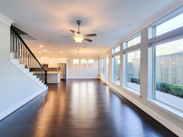 unfurnished living room featuring ceiling fan with notable chandelier, a healthy amount of sunlight, and ornamental molding