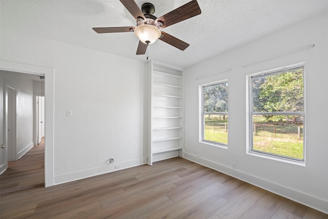 spare room featuring a textured ceiling, light hardwood / wood-style floors, built in features, and ceiling fan