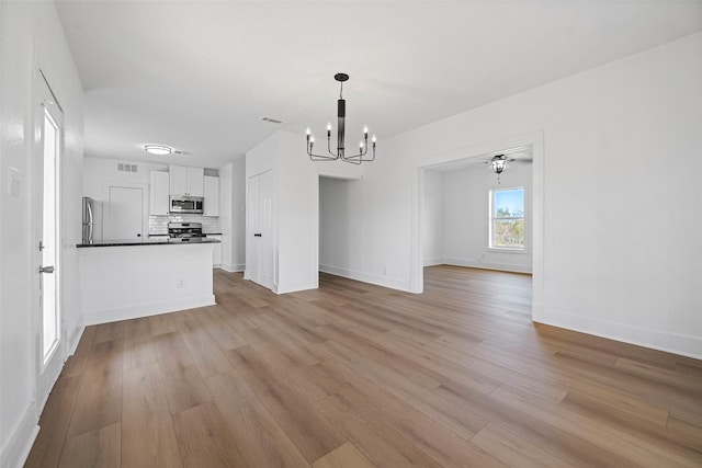 unfurnished living room with ceiling fan with notable chandelier and light hardwood / wood-style floors