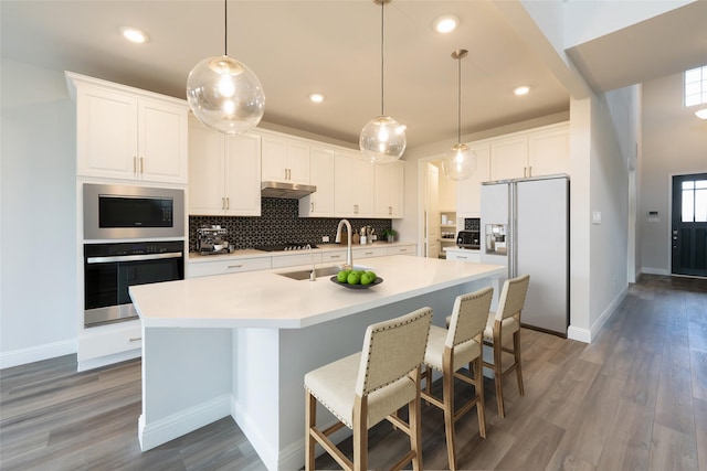 kitchen featuring white cabinets, stainless steel oven, white refrigerator with ice dispenser, and a kitchen island with sink