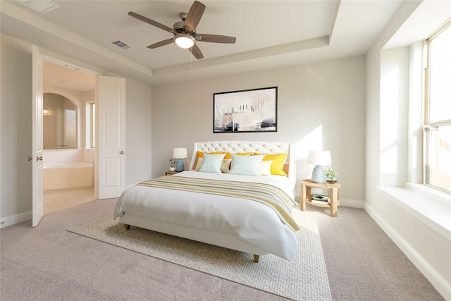 carpeted bedroom with a raised ceiling, multiple windows, ceiling fan, and connected bathroom