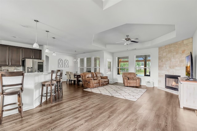 living room with a fireplace, wood-type flooring, a tray ceiling, and ceiling fan