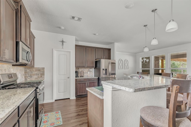 kitchen with decorative backsplash, a center island with sink, stainless steel appliances, and decorative light fixtures