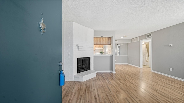 unfurnished living room with a fireplace, a textured ceiling, and light hardwood / wood-style flooring