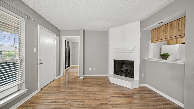 unfurnished living room with light hardwood / wood-style floors, a textured ceiling, and a brick fireplace