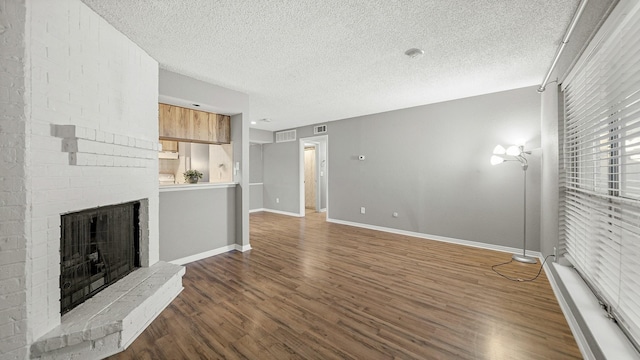 unfurnished living room featuring dark hardwood / wood-style flooring, a textured ceiling, and a brick fireplace