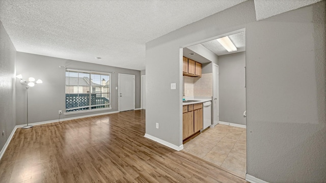 kitchen featuring backsplash, dishwasher, a textured ceiling, and light wood-type flooring