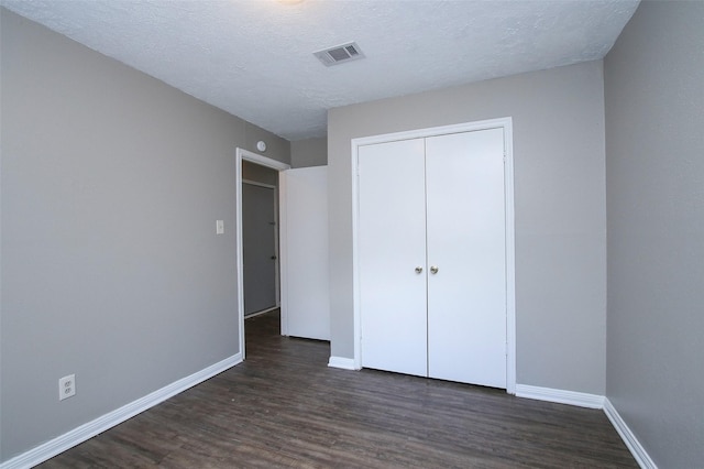 unfurnished bedroom featuring a textured ceiling, dark hardwood / wood-style flooring, and a closet