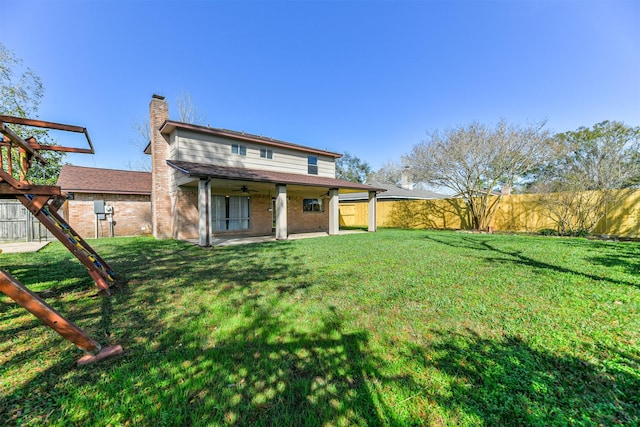 rear view of property with ceiling fan, a patio area, and a yard