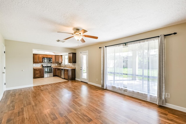 kitchen featuring backsplash, light hardwood / wood-style flooring, ceiling fan, a textured ceiling, and stainless steel appliances