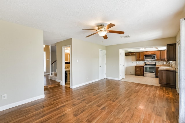 kitchen with ceiling fan, sink, stainless steel appliances, tasteful backsplash, and light wood-type flooring