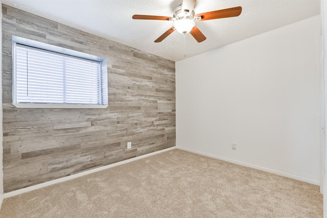 carpeted spare room featuring ceiling fan, wood walls, and a textured ceiling