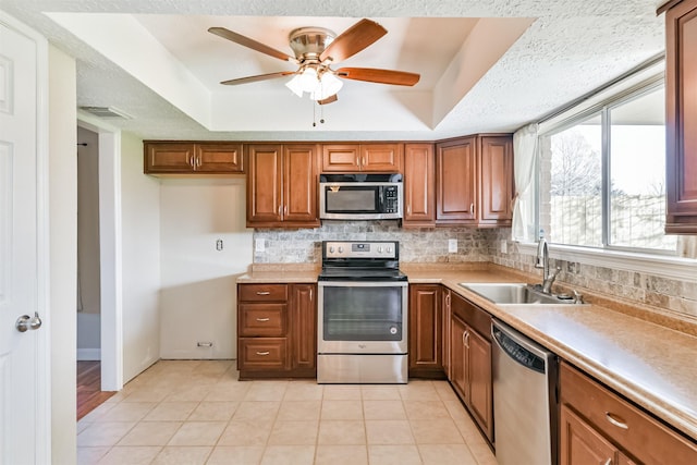 kitchen with appliances with stainless steel finishes, a tray ceiling, ceiling fan, sink, and light tile patterned floors