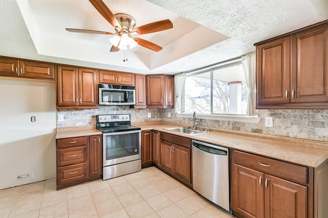 kitchen with ceiling fan, a raised ceiling, sink, and appliances with stainless steel finishes