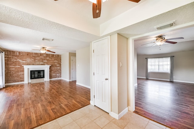 unfurnished living room with ceiling fan, a large fireplace, light tile patterned floors, and a textured ceiling