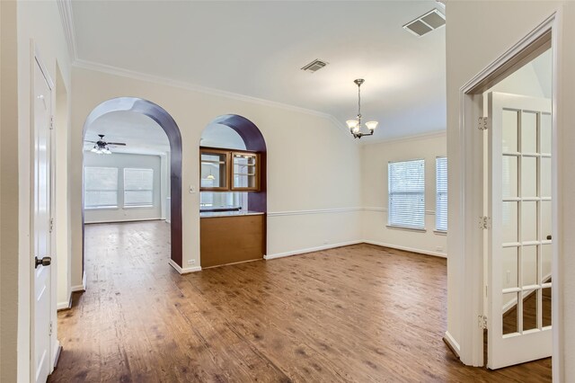 empty room featuring wood-type flooring, ceiling fan with notable chandelier, and ornamental molding