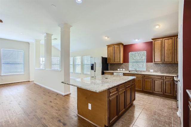 kitchen featuring ornate columns, light stone counters, a center island, stainless steel appliances, and decorative backsplash