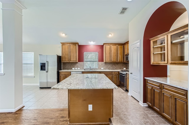 kitchen with a kitchen island, tasteful backsplash, sink, stainless steel appliances, and light stone countertops