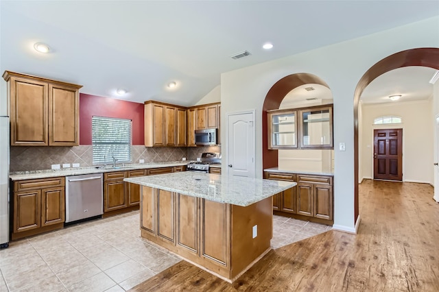 kitchen featuring sink, backsplash, stainless steel appliances, a center island, and light stone counters