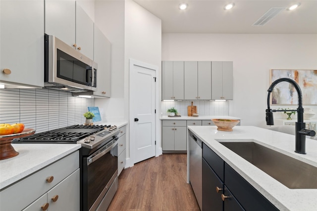 kitchen with hardwood / wood-style floors, sink, light stone countertops, tasteful backsplash, and stainless steel appliances