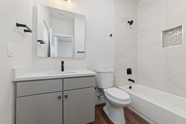 full bathroom featuring vanity, hardwood / wood-style floors, tiled shower / bath combo, and toilet