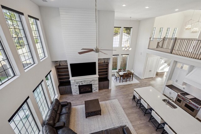 living room with a fireplace, a towering ceiling, light hardwood / wood-style flooring, and ceiling fan with notable chandelier