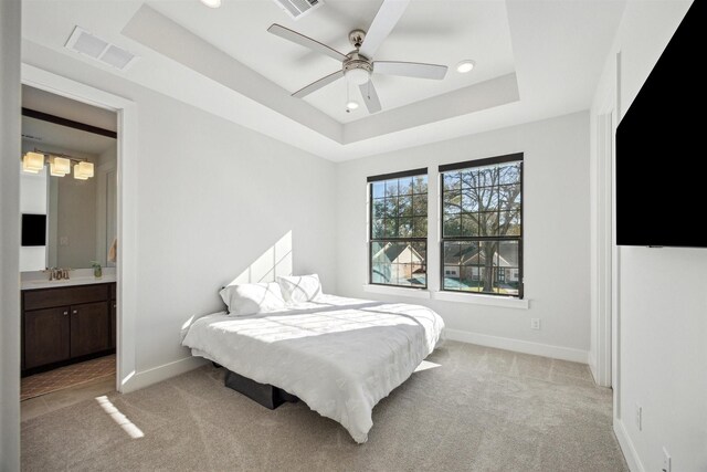 bedroom with light carpet, a raised ceiling, sink, ensuite bath, and ceiling fan