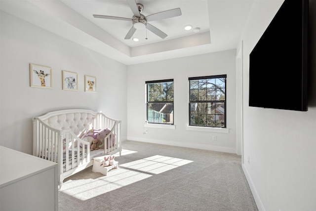 carpeted bedroom with ceiling fan, a crib, and a tray ceiling