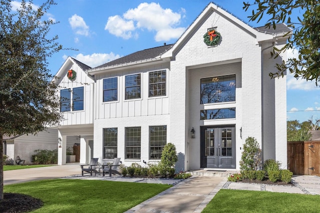 modern inspired farmhouse with fence, french doors, a front lawn, board and batten siding, and brick siding