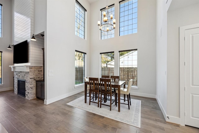 dining room with an inviting chandelier, wood-type flooring, a healthy amount of sunlight, and a brick fireplace