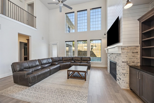 living room featuring a high ceiling, light wood-type flooring, a brick fireplace, and ceiling fan