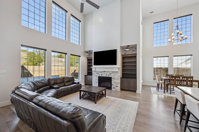 living area featuring ceiling fan with notable chandelier, a fireplace, wood finished floors, and baseboards