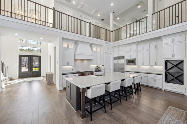 kitchen featuring custom range hood, sink, built in appliances, a high ceiling, and a large island