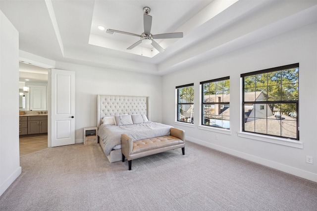 carpeted bedroom featuring a tray ceiling, ensuite bath, and ceiling fan