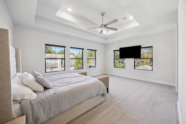 bedroom with ceiling fan, light carpet, and a tray ceiling