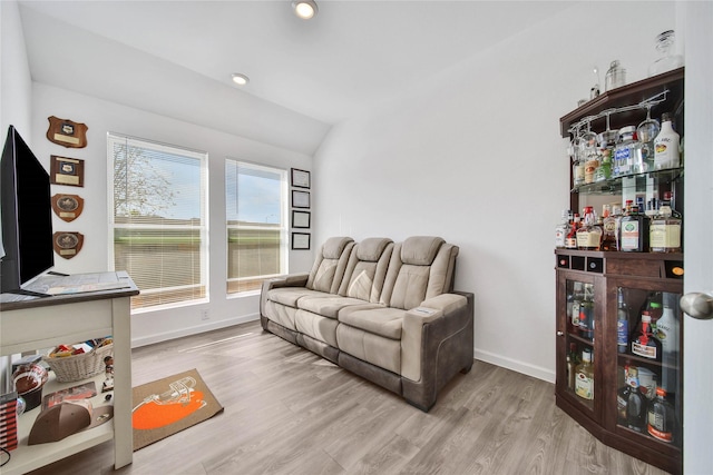 living room featuring bar, light hardwood / wood-style floors, and vaulted ceiling