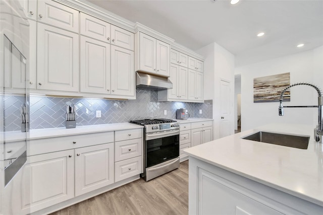 kitchen with sink, stainless steel range with gas cooktop, light hardwood / wood-style flooring, decorative backsplash, and white cabinets