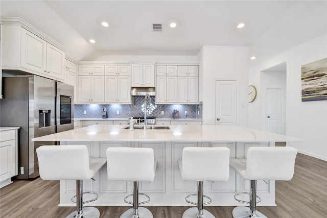 kitchen featuring stainless steel refrigerator with ice dispenser, a large island with sink, white cabinets, and a breakfast bar area