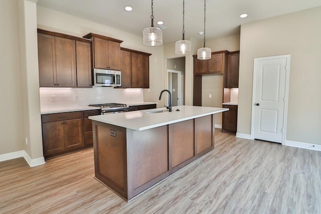 kitchen with sink, light wood-type flooring, an island with sink, appliances with stainless steel finishes, and decorative light fixtures