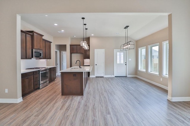 kitchen featuring sink, an island with sink, appliances with stainless steel finishes, decorative light fixtures, and light hardwood / wood-style floors