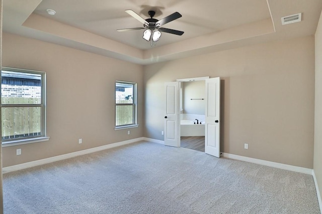 unfurnished bedroom with ceiling fan, a raised ceiling, and light carpet